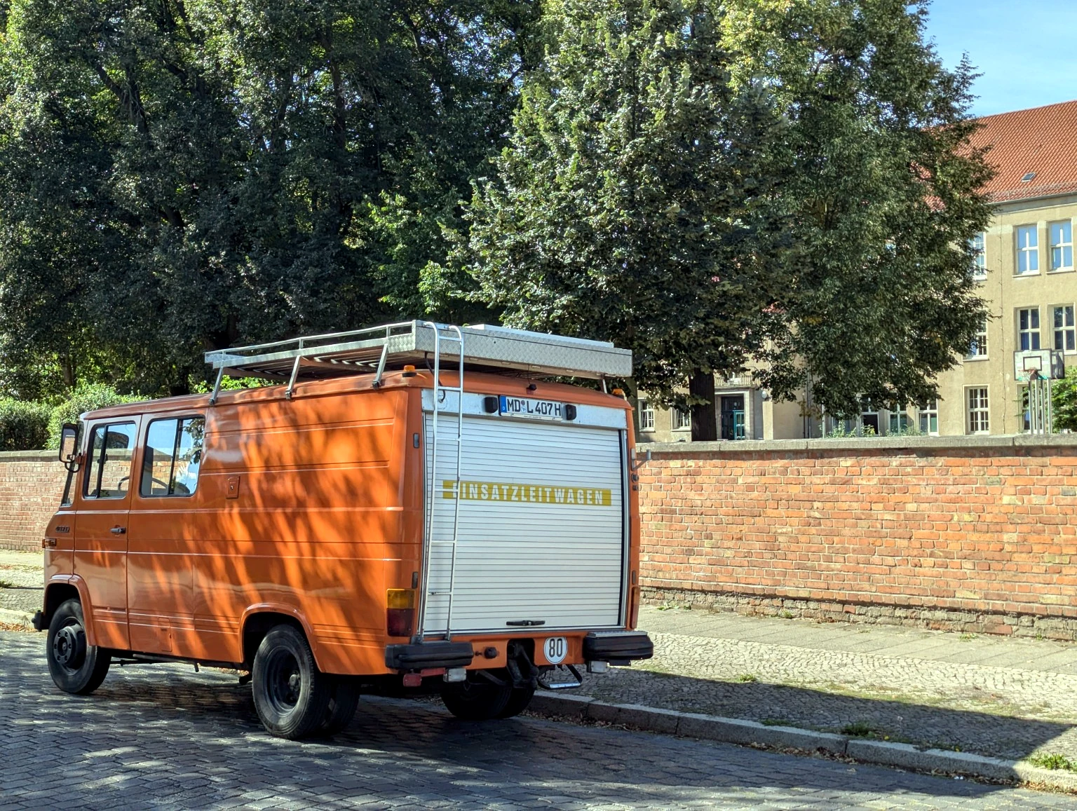Orangefarbener Mercedes Düdo von hinten und seitlich, der Rolladen ist geschlossen